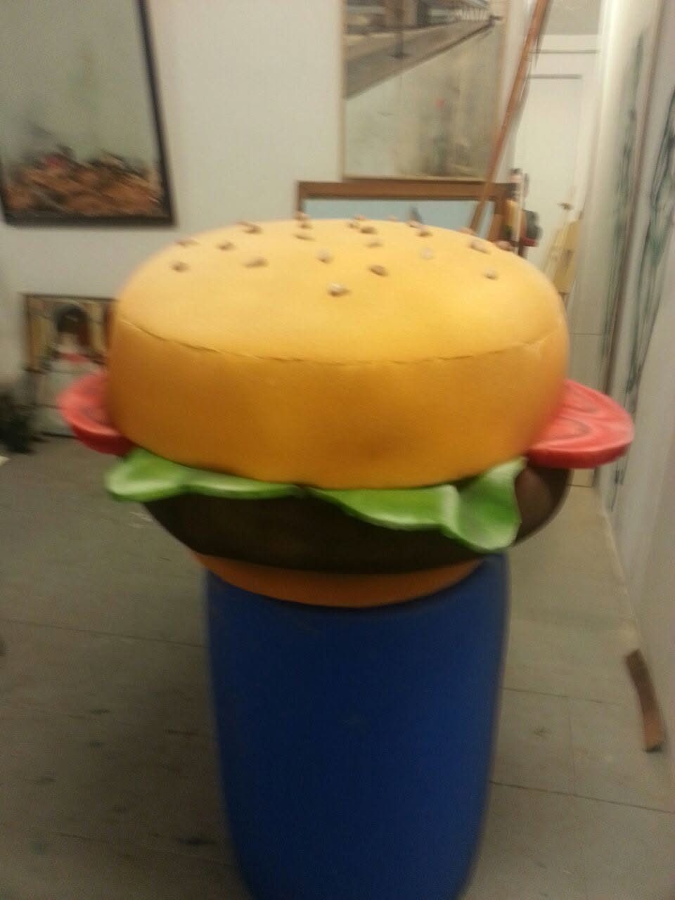 Figura gigante de una hamburguesa sobre un bidón azul